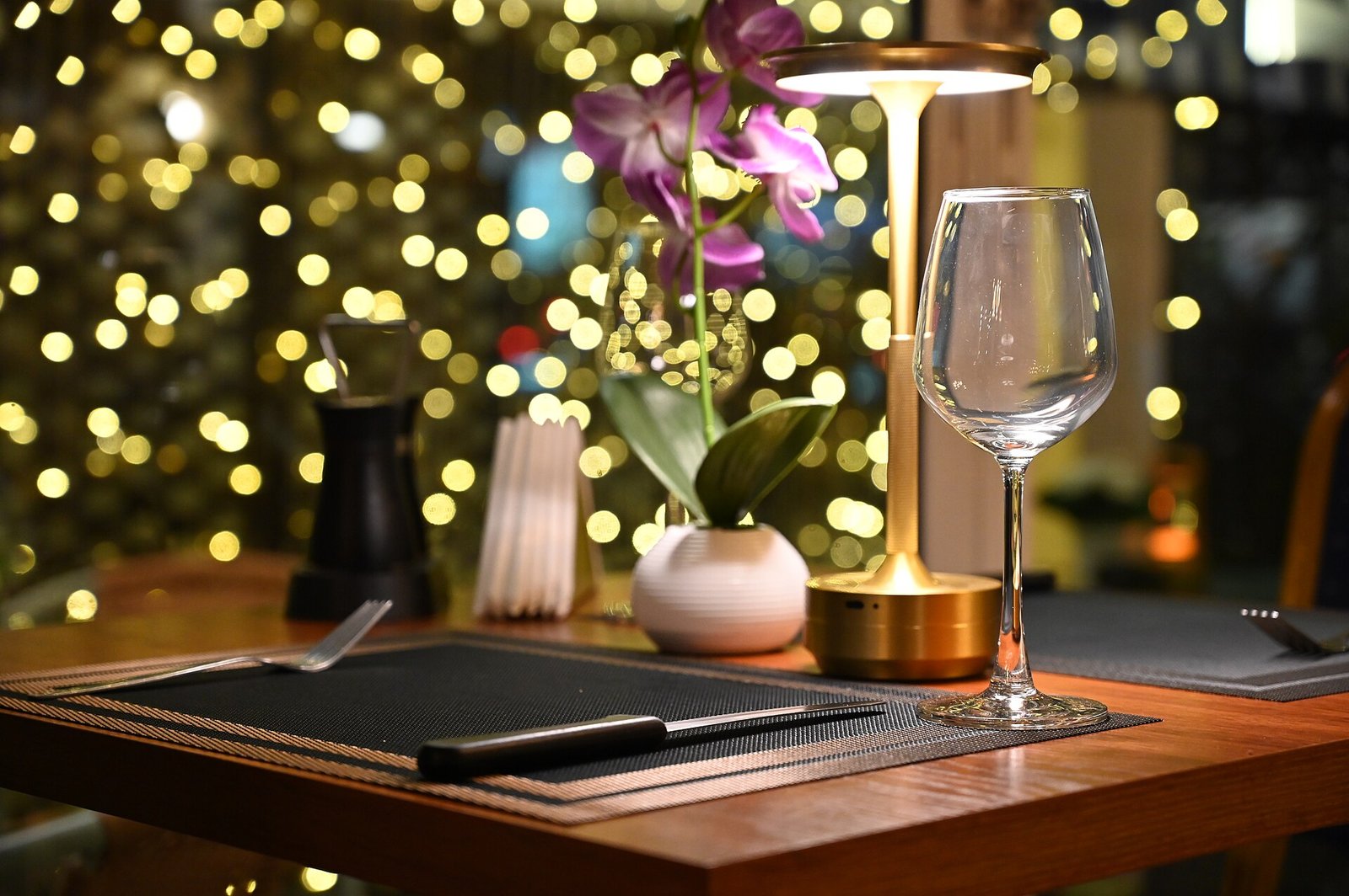 Mesa vestida con copa de vino, orquídea y lámpara de mesa, lista para el servicio.
