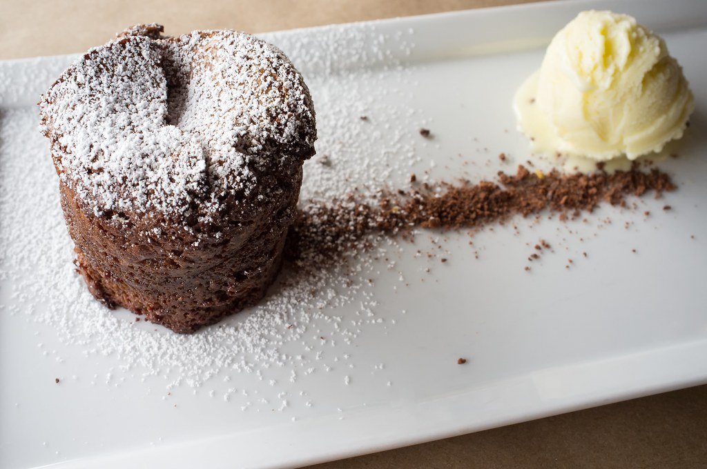 Pastel de chocolate espolvoreado con azúcar glas, acompañado de una quenelle de helado de vainilla.