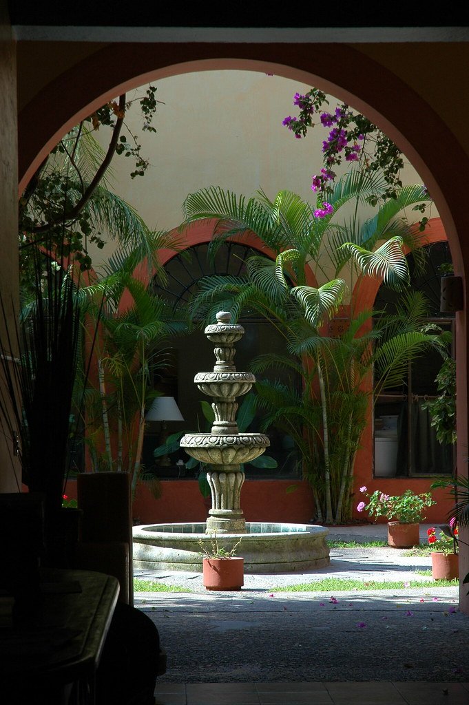 Patio de hacienda visto desde el arco de acceso, con fuente de cantera y jardín