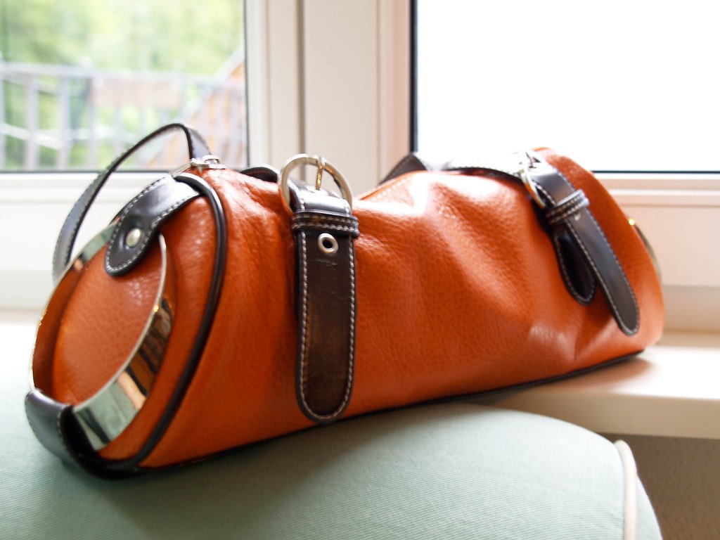 Bolso de piel color coñac con asas trenzadas junto a una ventana