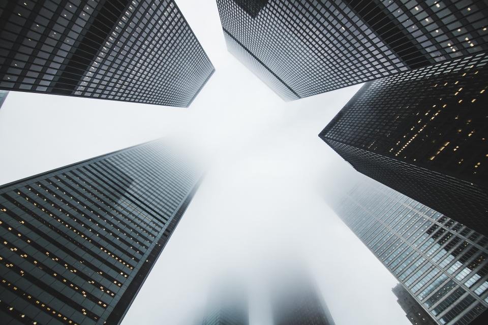 Fachada de vidrio de una torre corporativa vista en contrapicado, con retícula de perfiles verticales