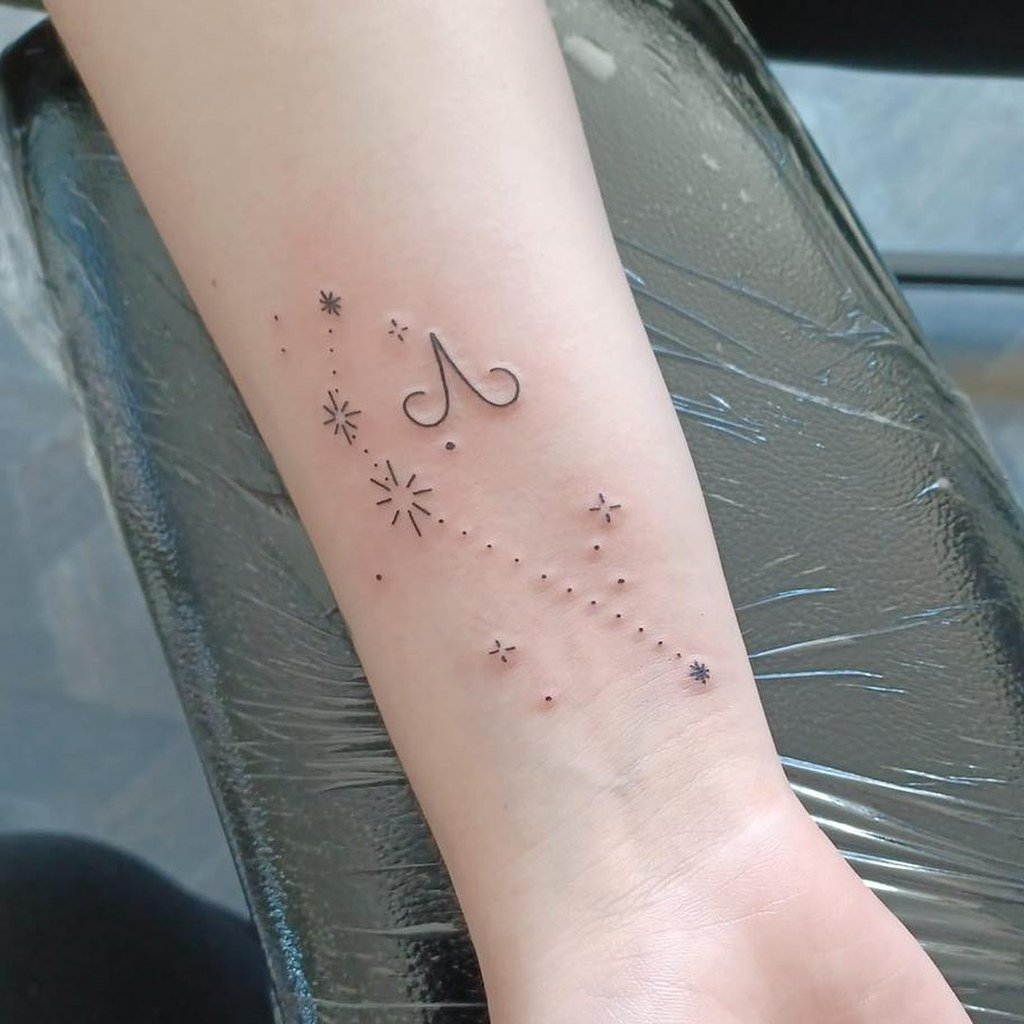 Símbolo zodiacal y estrellas de trazo fino tatuados en el antebrazo